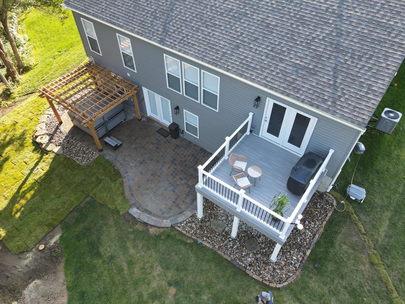 Aerial view of a patio under a white deck, with a pergola beside it and a rock border
