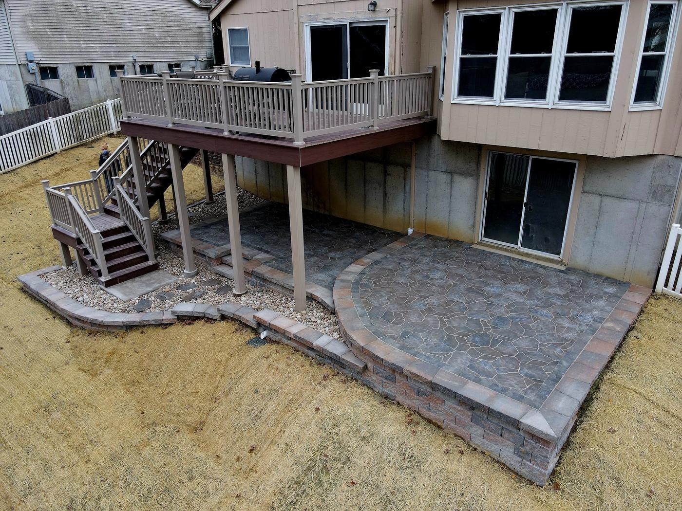 A new paver patio under a raised deck, with a curved extension and a border