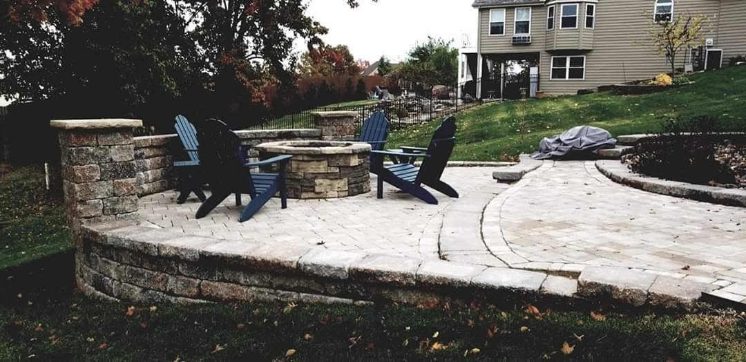 A finished patio with a seating wall and Adirondack chairs round a fire pit, late light