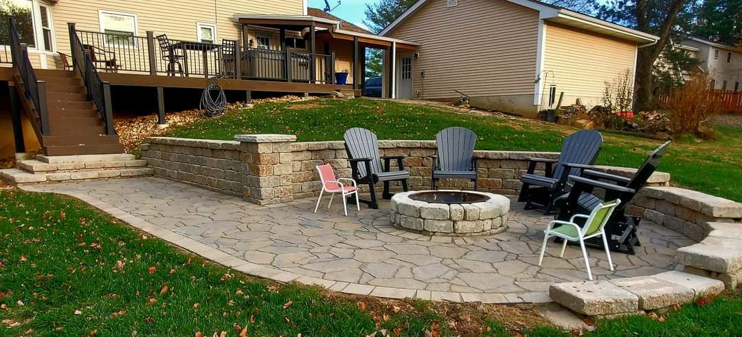 A finished patio with a seating wall, a fire pit and Adirondack chairs, with a deck behind