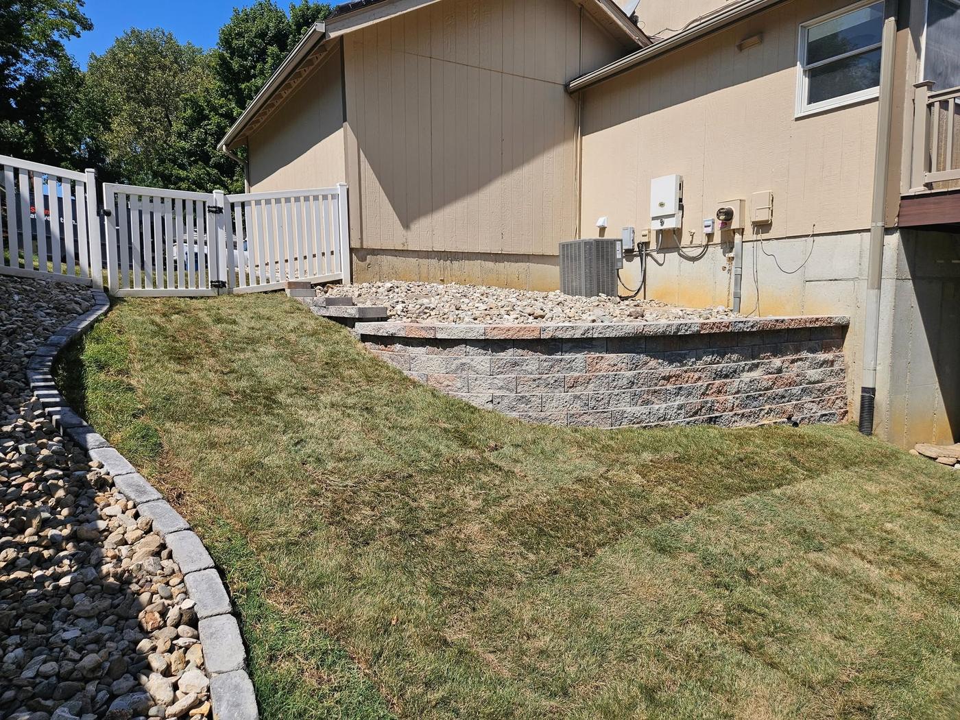 A new raised block wall bed at the back of a yard with a rock edge