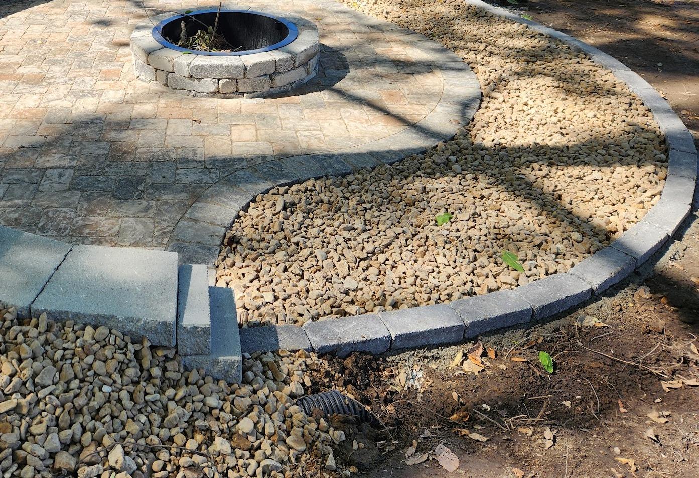 A sunken round patio behind a curved seating wall, with a fire pit and a rock surround