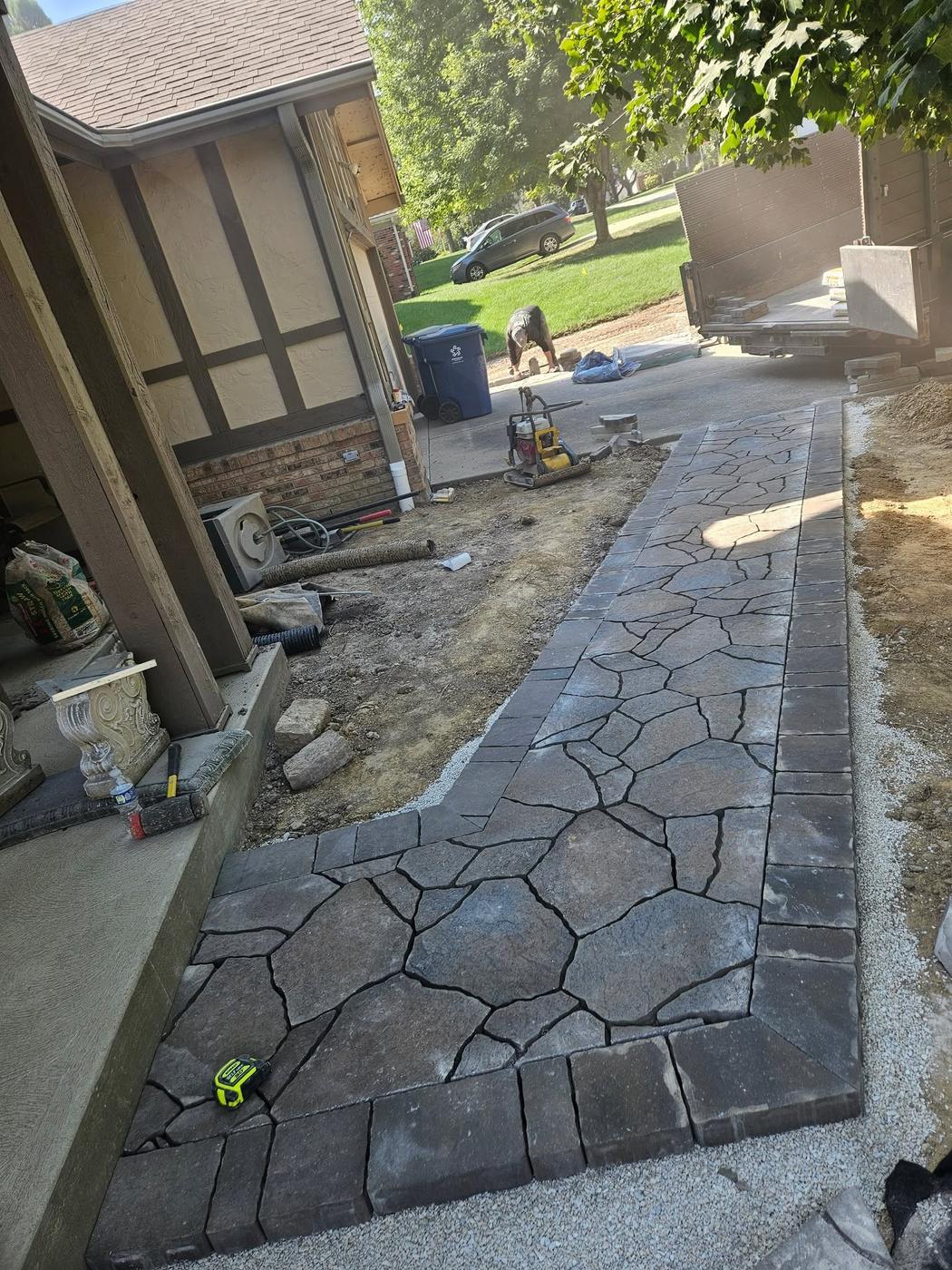 A flagstone-pattern walkway with a dark border beside a house, partway through the build