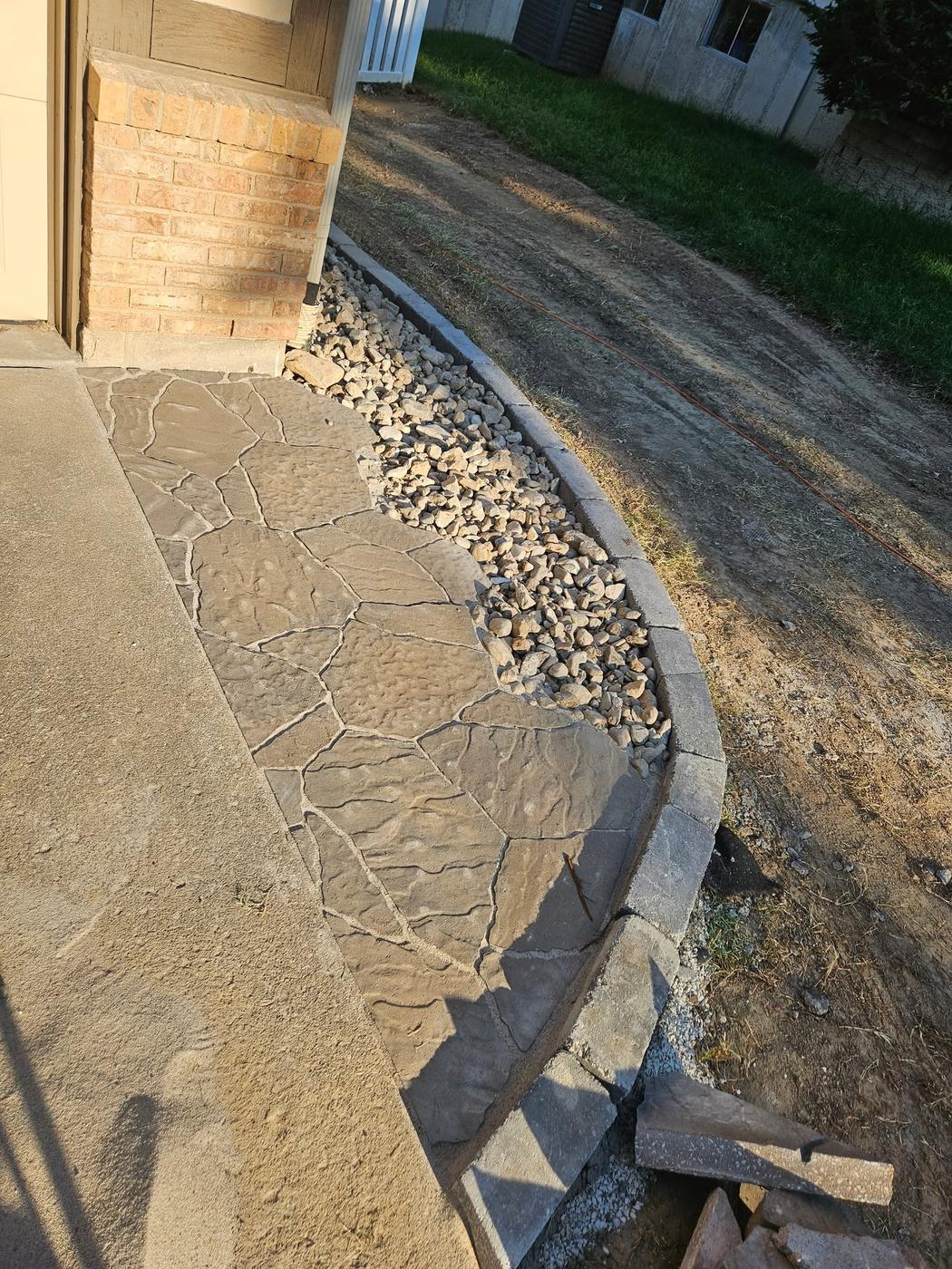 A flagstone-pattern walkway with a rock bed and edging, partway through the build